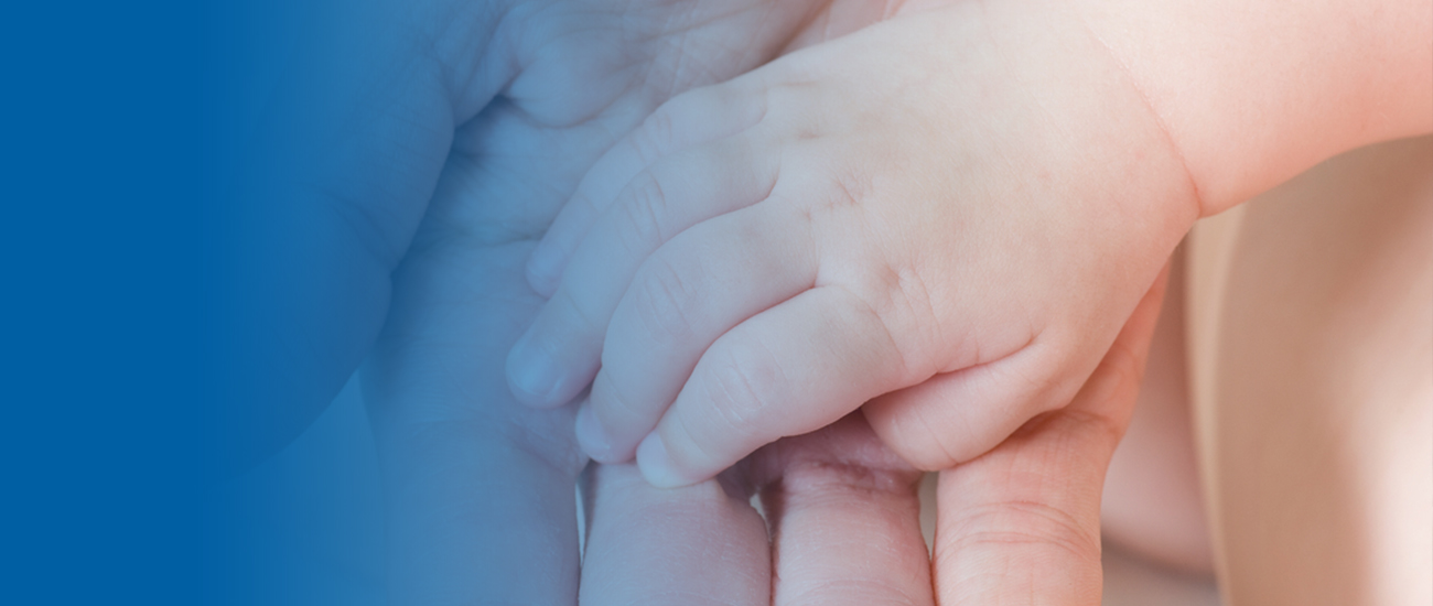 Photograph of a baby's hand with the palm facing down on top of a father's hand with the palm facing up. There is a blue gradient extending to the left that becomes fainter as it progresses until it is entirely blue.